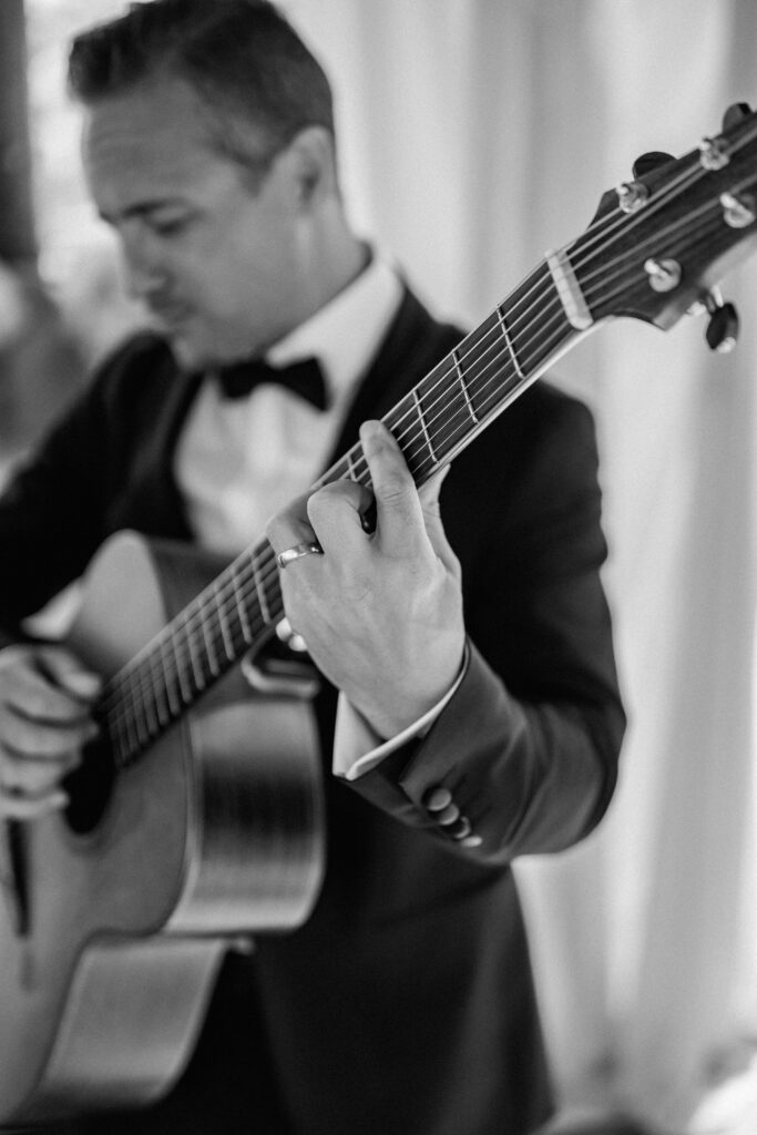 Ein Mann in Anzug und Fliege spielt auf einer Akustikgitarre