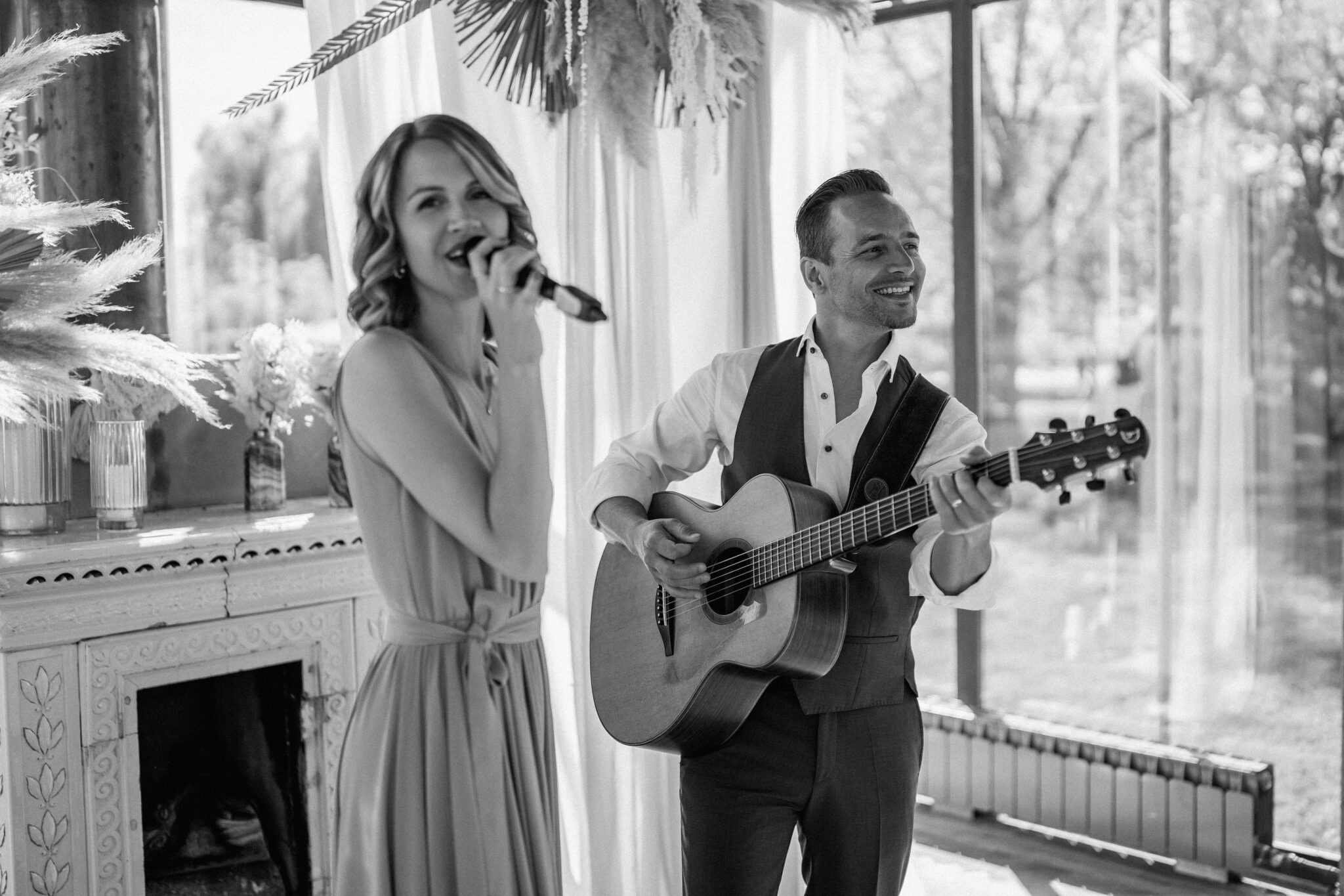 Eine Frau tritt als Hochzeitssängerin in einem eleganten, hellen Raum auf, während ein Mann sie auf der Gitarre begleitet - perfekt für stilvolle Feiern in Südtirol oder der Schweiz.