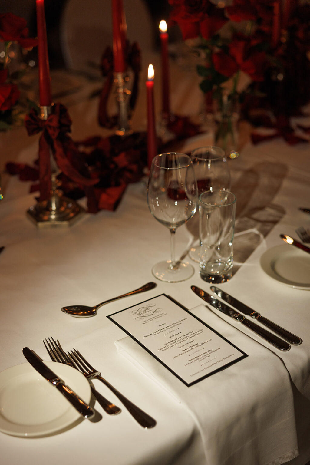 Elegante Tafel mit roten Kerzen, Rosen, Gläsern und einem Menü auf einer weißen Tischdecke - perfekt für einen Trauredner oder Hochzeitsmusiker bei einer romantischen Feier in Süddeutschland.